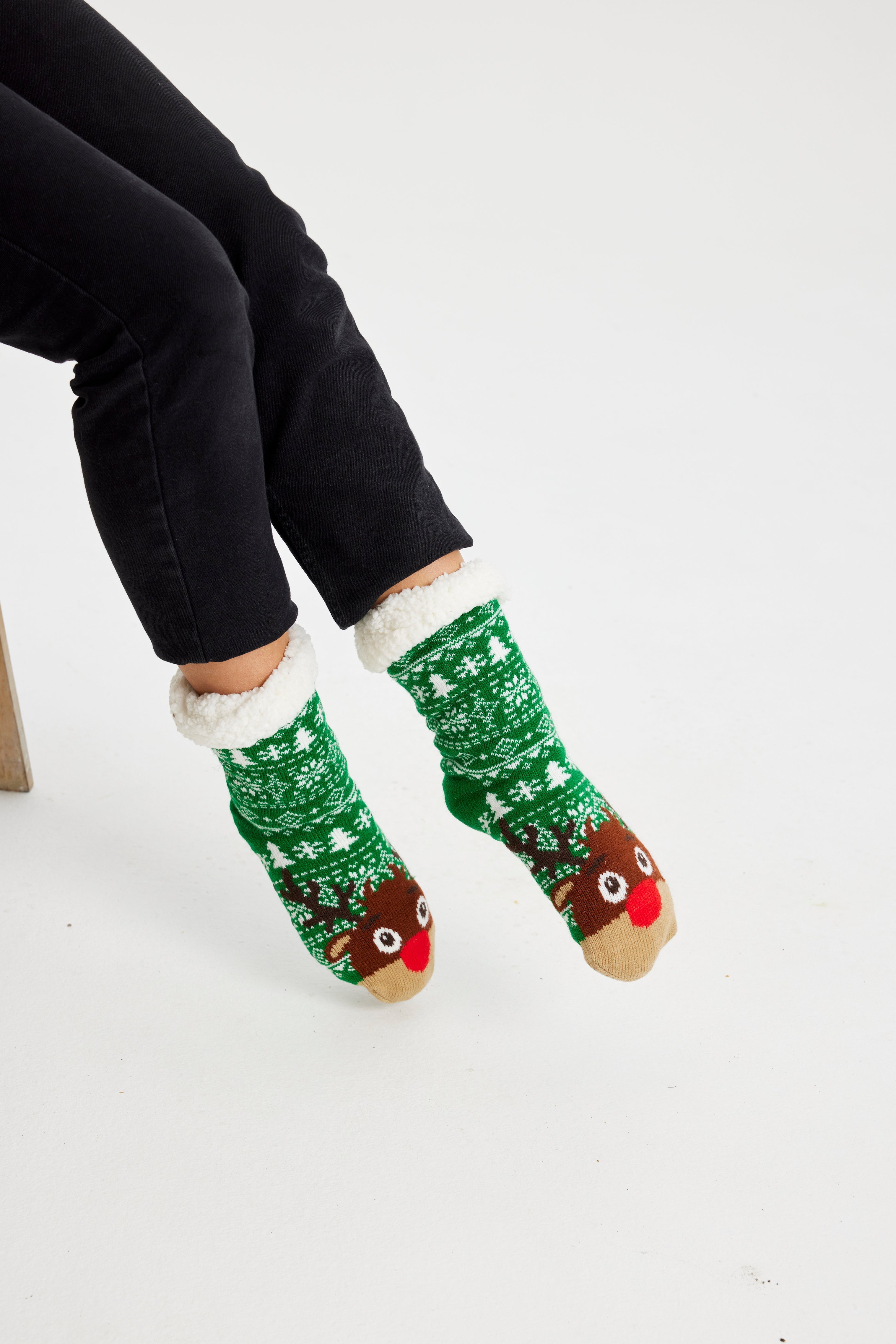 Ein Paar Beine, die ein Paar grüne Weihnachtssocken mit einem Rentier darauf tragen.